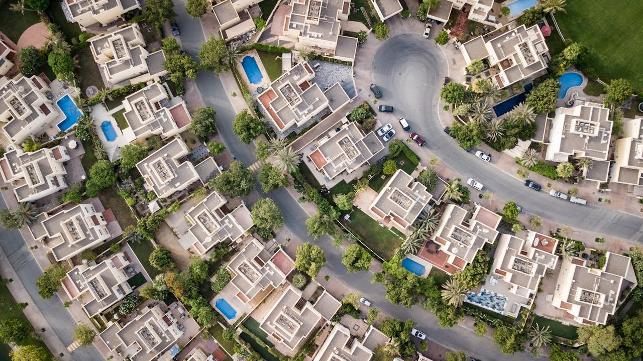 Home Explore a stunning aerial view of a residential area in Dubai with lush greenery and swimming pools.