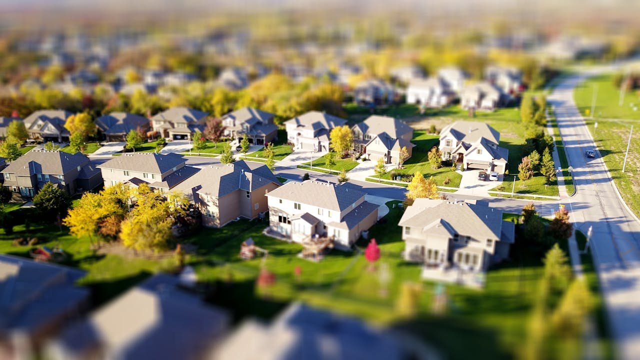 Offerings Tilt-shift aerial photo of a suburban neighborhood with green lawns and roads.