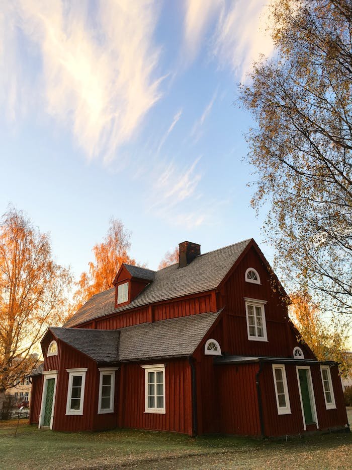 Home Picturesque red wooden house in autumn. Traditional Swedish architecture amidst colorful foliage.